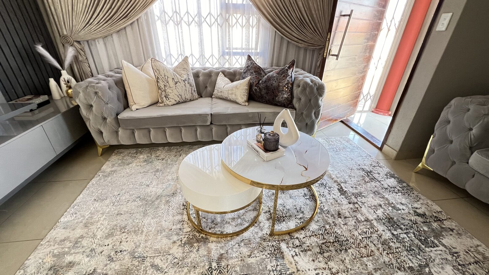 Tufted grey velvet chesterfield couch with gold nesting coffee tables by Nto Interiors